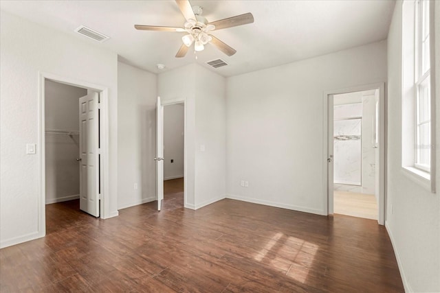 unfurnished bedroom with ensuite bath, dark wood-style flooring, a walk in closet, and visible vents