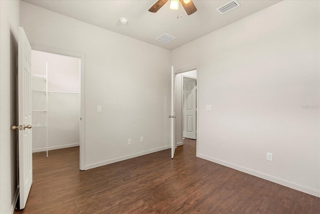 unfurnished bedroom with a spacious closet, wood finished floors, visible vents, and baseboards