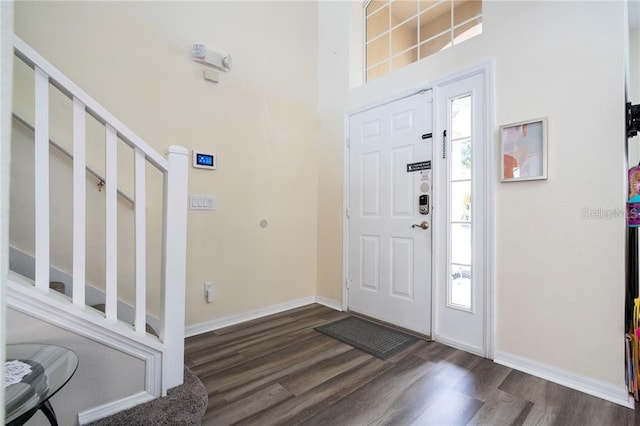 foyer entrance with baseboards, plenty of natural light, a towering ceiling, and dark wood-style floors