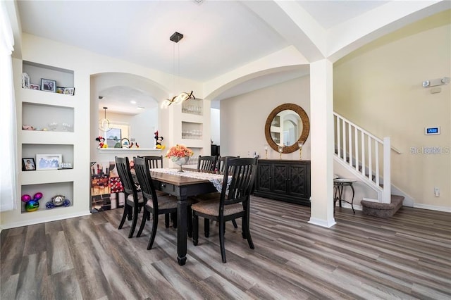 dining room featuring built in shelves, arched walkways, wood finished floors, and stairs