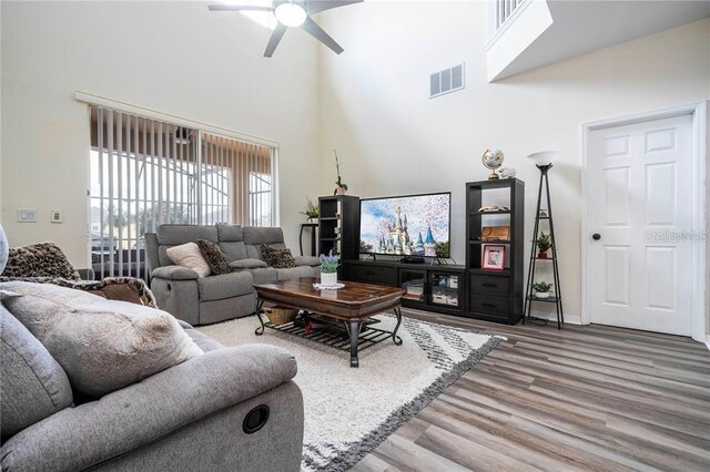 living room featuring a towering ceiling, wood-type flooring, and ceiling fan