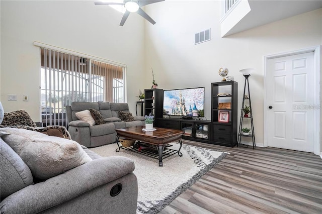 living room with a high ceiling, wood finished floors, visible vents, a ceiling fan, and baseboards