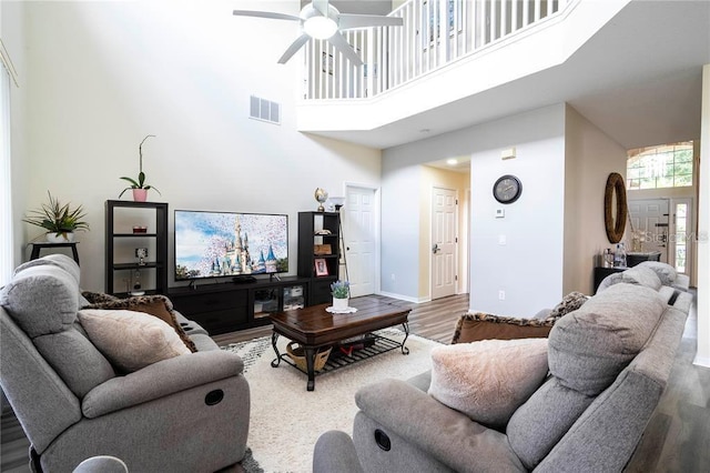 living room with a high ceiling, ceiling fan, and wood-type flooring