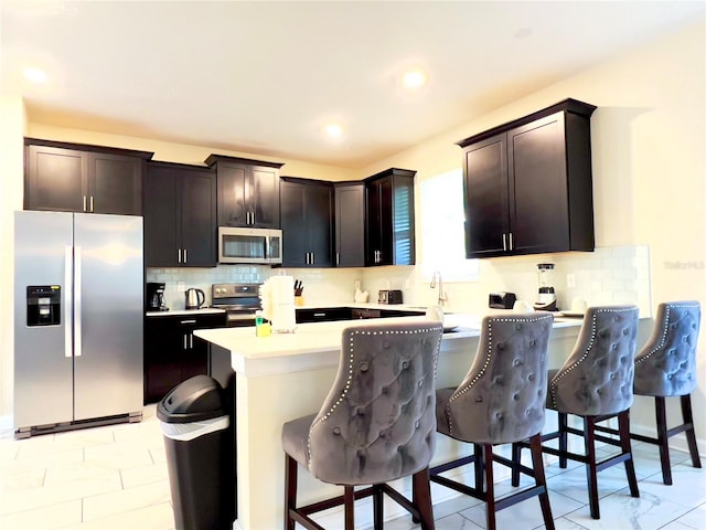 kitchen featuring appliances with stainless steel finishes, dark brown cabinets, a kitchen bar, and kitchen peninsula