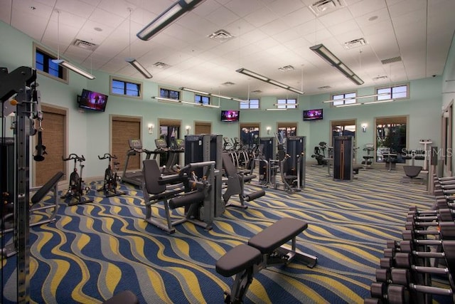 exercise room featuring a healthy amount of sunlight, carpet, and a towering ceiling