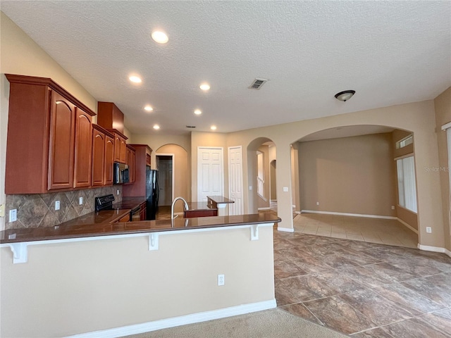 kitchen with kitchen peninsula, backsplash, a breakfast bar, a textured ceiling, and black appliances