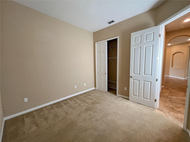 unfurnished bedroom with a closet, light colored carpet, and a textured ceiling