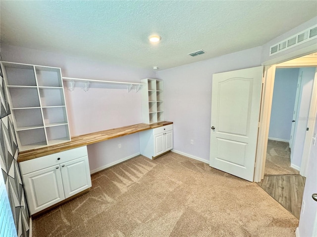 unfurnished office with built in desk, light carpet, and a textured ceiling