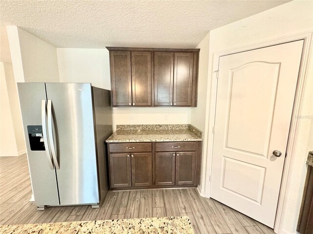 kitchen with light hardwood / wood-style flooring, light stone counters, stainless steel refrigerator with ice dispenser, dark brown cabinetry, and a textured ceiling