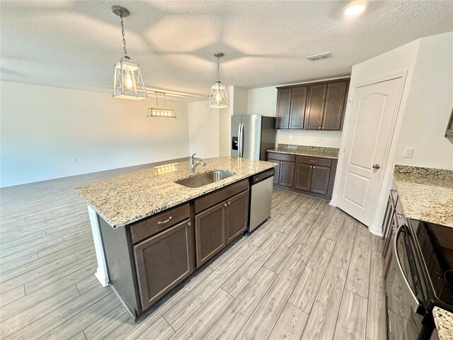 kitchen featuring light wood-type flooring, appliances with stainless steel finishes, light stone counters, sink, and a textured ceiling