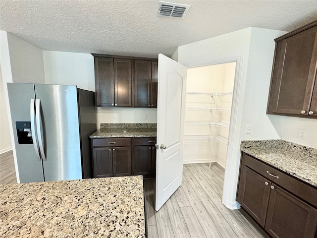 kitchen with light wood-type flooring, light stone countertops, stainless steel fridge with ice dispenser, and dark brown cabinetry