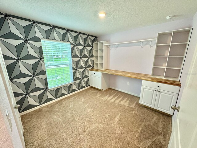 unfurnished office with built in desk, light carpet, and a textured ceiling