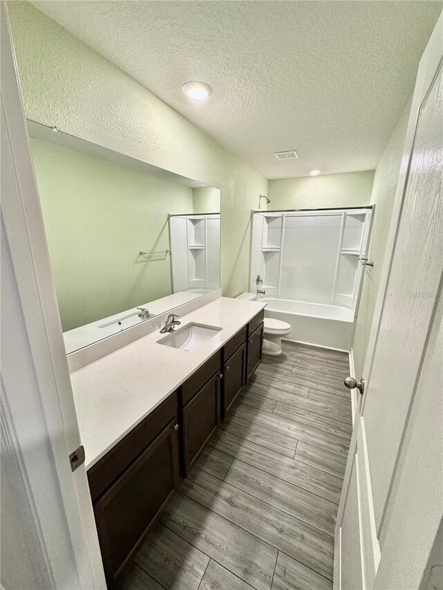 full bathroom featuring toilet, vanity, a textured ceiling, bathtub / shower combination, and wood-type flooring