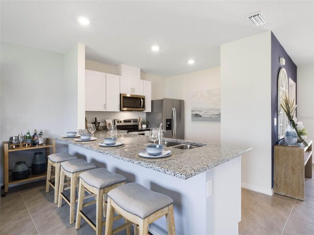 kitchen featuring light tile patterned floors, kitchen peninsula, light stone countertops, appliances with stainless steel finishes, and a breakfast bar area