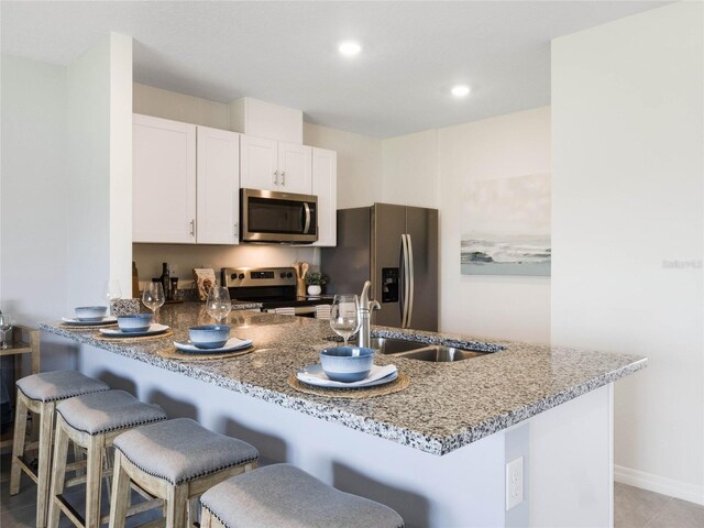 kitchen with stone countertops, appliances with stainless steel finishes, a kitchen bar, kitchen peninsula, and white cabinets