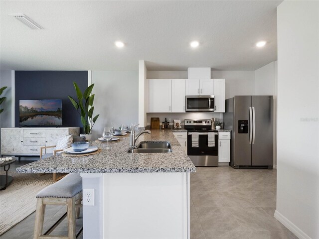 kitchen with appliances with stainless steel finishes, light stone counters, white cabinetry, sink, and a kitchen bar