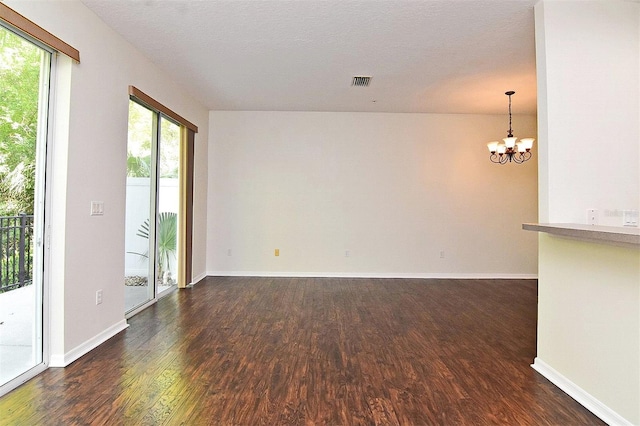 spare room with a textured ceiling, a notable chandelier, and dark hardwood / wood-style flooring