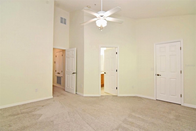 empty room featuring light colored carpet, a high ceiling, and ceiling fan