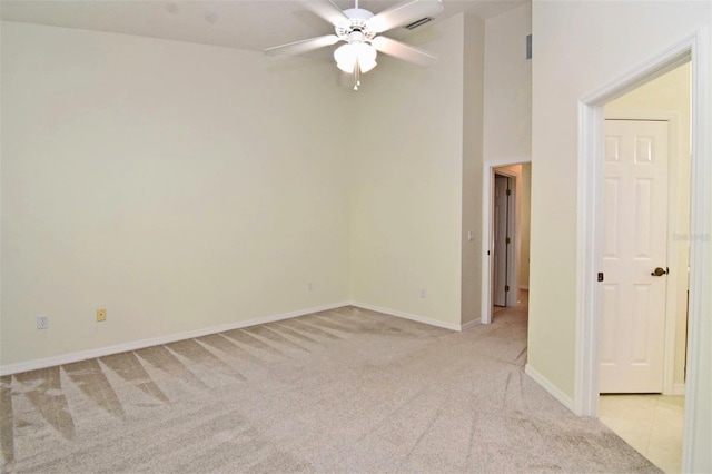 empty room featuring ceiling fan, light carpet, and a high ceiling