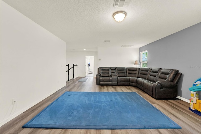 living area with a textured ceiling, wood finished floors, visible vents, and baseboards