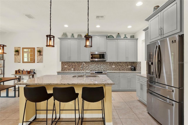 kitchen featuring a kitchen island with sink, sink, light stone countertops, decorative light fixtures, and stainless steel appliances