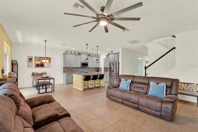 tiled living room with ceiling fan with notable chandelier