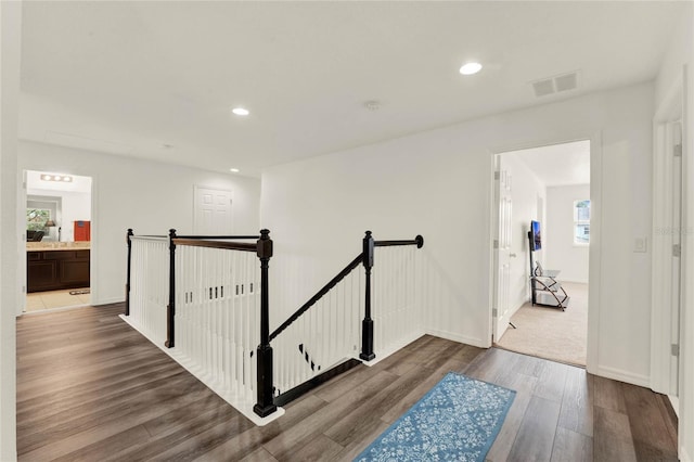 hallway with recessed lighting, wood finished floors, visible vents, baseboards, and an upstairs landing