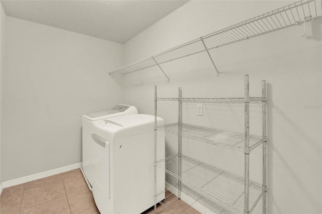 laundry room featuring light tile patterned floors, a textured ceiling, laundry area, baseboards, and washer and clothes dryer