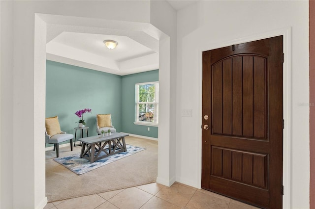 foyer featuring a tray ceiling, light carpet, baseboards, and light tile patterned flooring