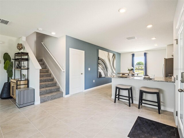 kitchen with light tile patterned floors, stone countertops, stainless steel fridge, kitchen peninsula, and a kitchen bar