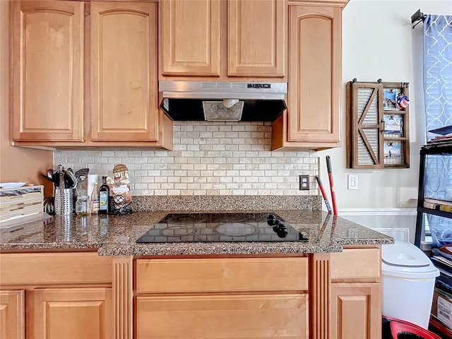 kitchen featuring ventilation hood, decorative backsplash, dark stone countertops, light brown cabinetry, and black stovetop