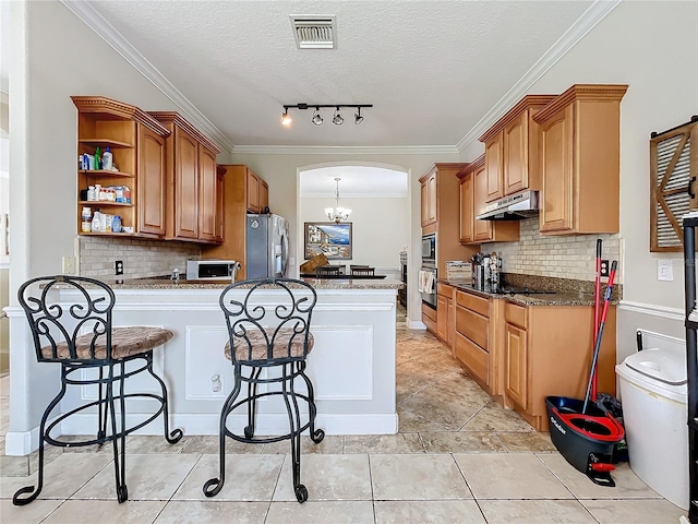 kitchen with a textured ceiling, backsplash, appliances with stainless steel finishes, ornamental molding, and dark stone countertops