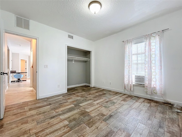 unfurnished bedroom with light wood-type flooring, a textured ceiling, and a closet