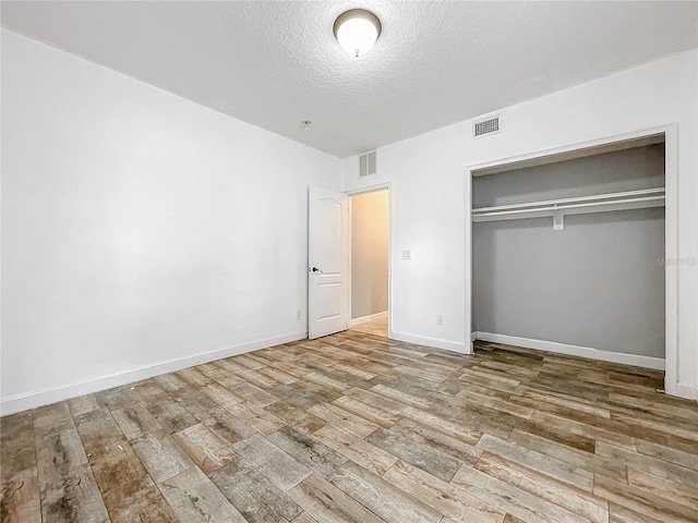 unfurnished bedroom featuring a textured ceiling, a closet, and light hardwood / wood-style floors