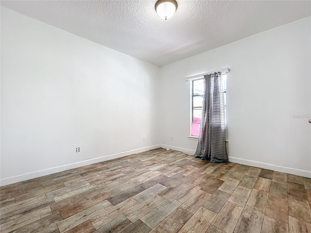 empty room with a textured ceiling and light hardwood / wood-style flooring