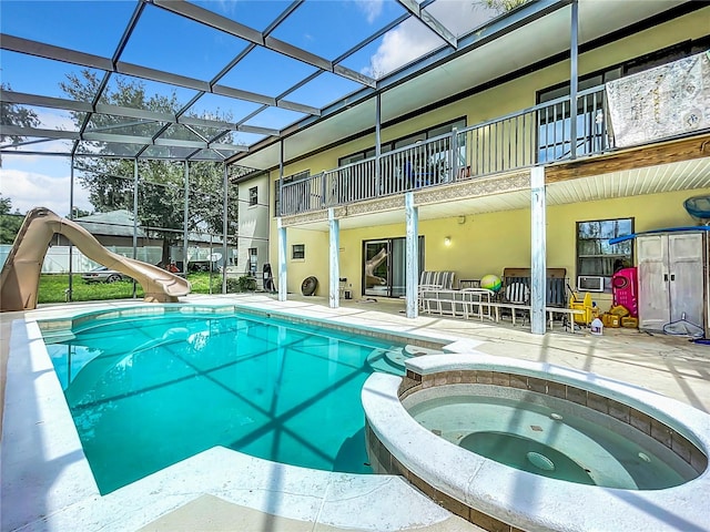 view of pool with a lanai, a water slide, an in ground hot tub, and a patio area