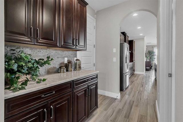 bar with arched walkways, baseboards, decorative backsplash, light wood finished floors, and stainless steel fridge