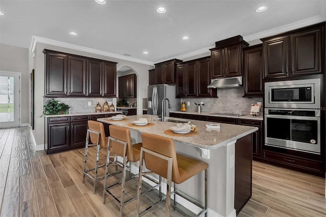 kitchen with stainless steel appliances, a breakfast bar, wood finish floors, and under cabinet range hood