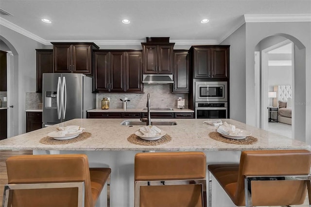 kitchen with arched walkways, appliances with stainless steel finishes, a sink, and under cabinet range hood