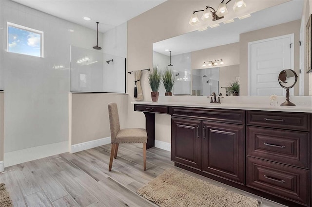 bathroom featuring wood finished floors, walk in shower, vanity, and baseboards