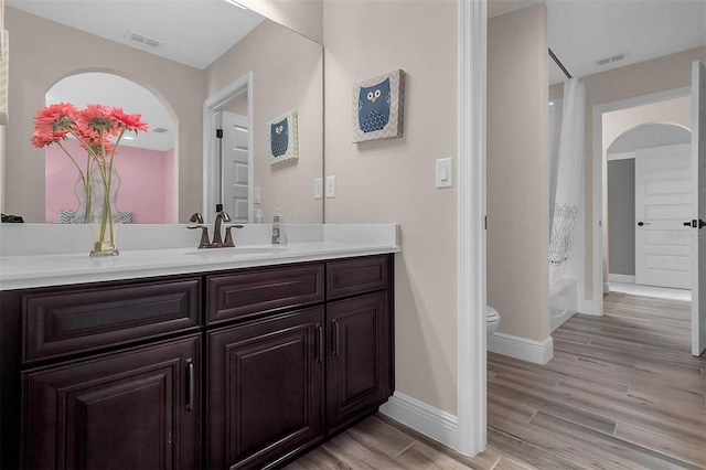 bathroom with visible vents, toilet, wood finished floors, shower / bathtub combination with curtain, and vanity