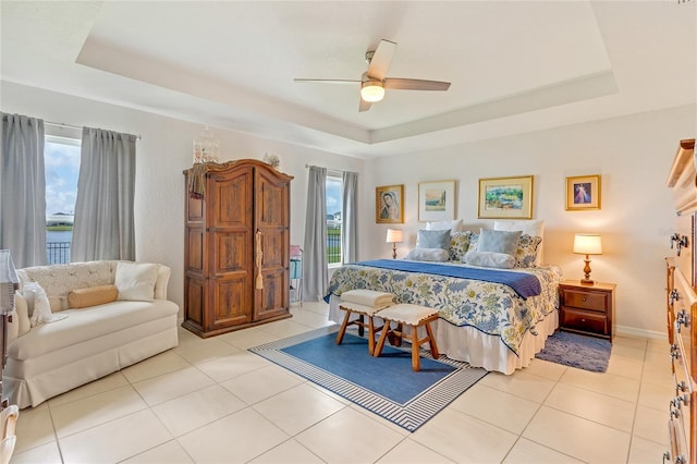 tiled bedroom featuring a tray ceiling, ceiling fan, and a water view