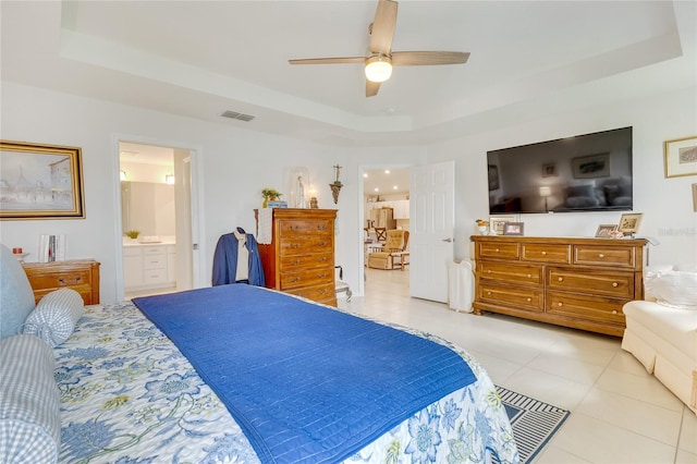 bedroom featuring a raised ceiling, ensuite bath, ceiling fan, and light tile patterned floors