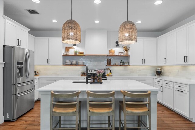 kitchen with white cabinets, a kitchen breakfast bar, stainless steel appliances, a center island with sink, and dark hardwood / wood-style flooring