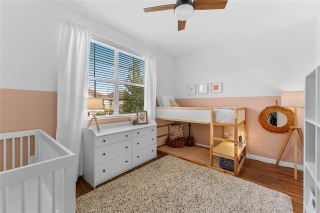 bedroom with ceiling fan, a nursery area, and wood-type flooring