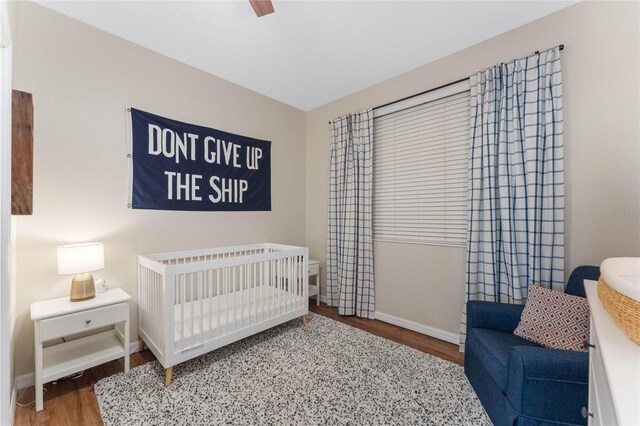 bedroom with hardwood / wood-style floors, ceiling fan, and a nursery area