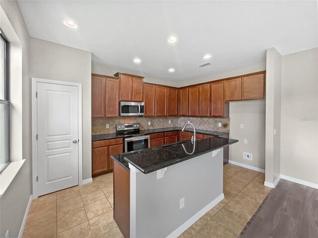 kitchen with dark stone countertops, appliances with stainless steel finishes, sink, a kitchen island with sink, and a breakfast bar