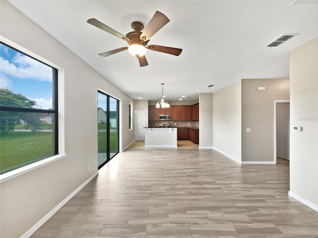 unfurnished living room featuring ceiling fan with notable chandelier and light hardwood / wood-style floors