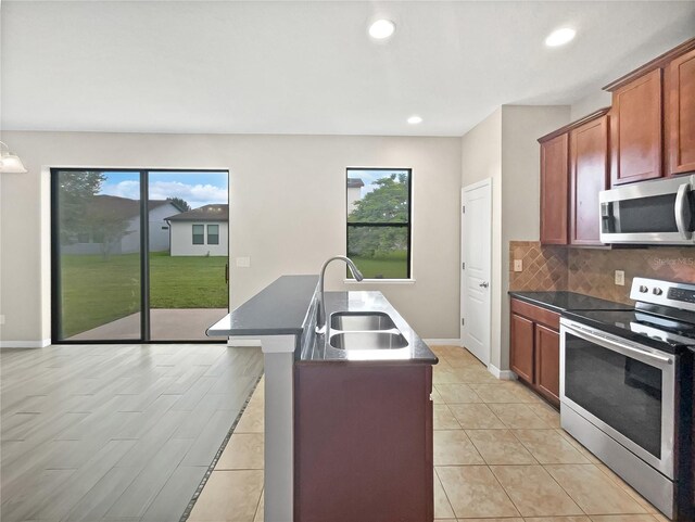 kitchen featuring a wealth of natural light, sink, appliances with stainless steel finishes, and a kitchen island with sink