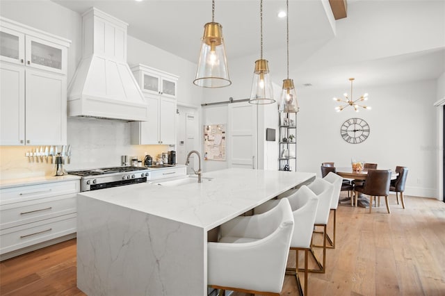 kitchen featuring a barn door, custom range hood, white cabinets, and light hardwood / wood-style floors